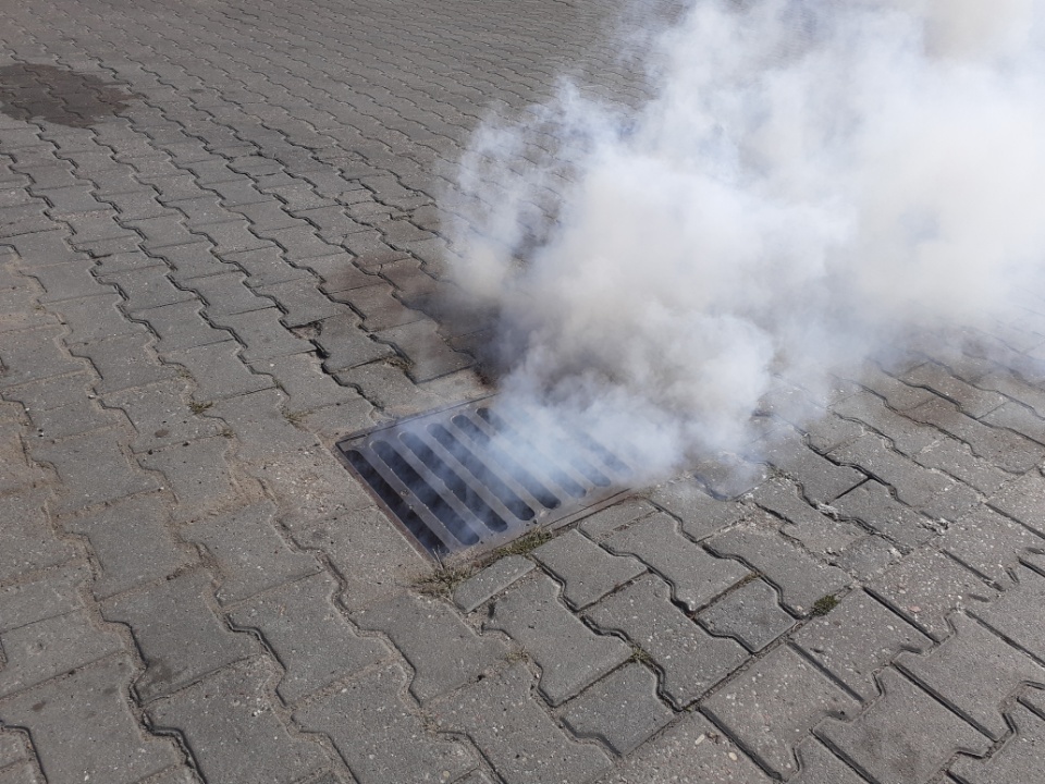 Wydobywający się dym z kratki ściekowej wskazuje nielegalne podłączenie placu do kanalizacji sanitarnej
